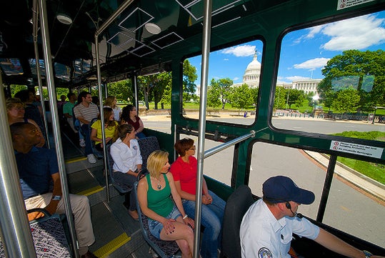 Passengers sit inside a tour bus as it drives past the United States Capitol building on a sunny day.