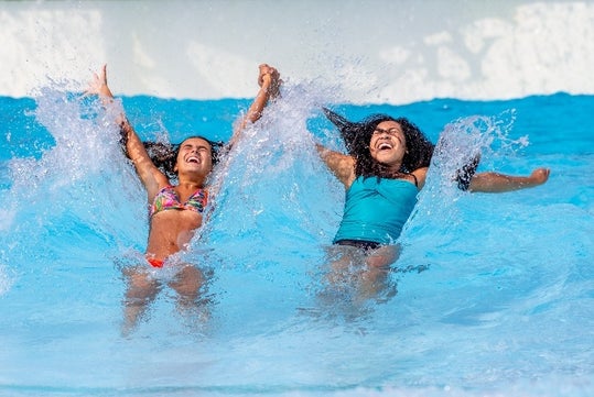 Two young girls dressed in a swim attire hold each other as they get splashed by artificial waves in a blue giant wave pool at Water Country in Portsmouth, New Hampshire.