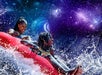 Two people ride a red inflatable raft on a water slide, splashing water, with a background resembling outer space and stars.