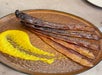 Five strips of crispy bacon are arranged on a brown plate with a smear of yellow sauce beside them.