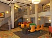 Lobby area with orange chairs around a central table, a staircase to the left, art on the walls, and a ceiling light fixture.