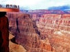 Visitors stand on a glass viewing platform overlooking the Grand Canyon's vast, layered rock formations.