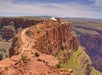 Tourists walk along a trail on the edge of a large canyon with a small building and canopy visible in the background.