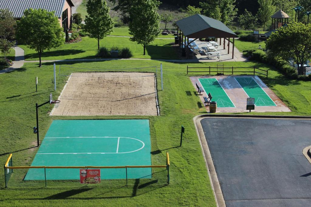 Aerial view of an outdoor recreation area featuring a sand volleyball court, a green basketball court, and a shaded picnic pavilion, surrounded by trees and grass.