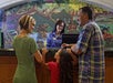 A family checks in at a hotel front desk, with a mural of a forest scene in the background.