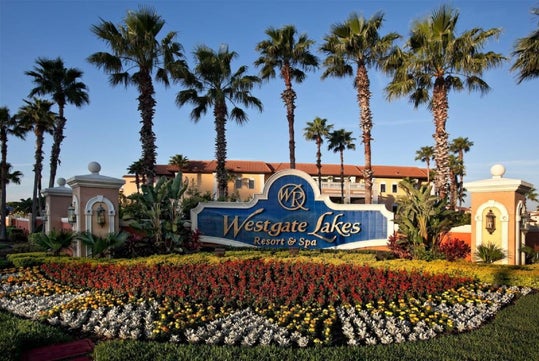 Entrance sign for Westgate Lakes Resort & Spa, surrounded by palm trees and a landscaped garden with colorful flowers.