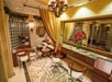 Elegant salon interior with two salon chairs, a large mirror, a manicure station, and decorative plants. Marble flooring features intricate designs. Warm lighting and a chandelier create a cozy atmosphere.