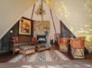 A cozy tent interior with rustic furniture, patterned rug, stone fireplace, western-themed decor, and antler chandelier.