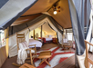 A spacious canvas tent features a bed, wooden rocking chairs, a patterned rug, and ceiling fan, blending rustic decor with modern comforts.