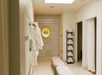 A spa changing room with a bench, robe on a hook, round mirror, and shelves stocked with rolled towels.