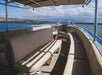 Empty beige seats on a covered boat deck, overlooking the water and a rocky shoreline under a partly cloudy sky.