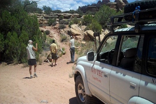 A white NAVTEC SUV parked with hikers on their way to start their White Rim Trail in Canyonlands National Park.