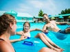 A man, woman, and child relax on blue pool floats in a sunny outdoor water park, smiling and holding onto each other's floats.