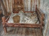 A rustic wooden bed frame with a thin mattress filled with straw, covered by a rough cloth, sits on a wooden floor in a weathered room.