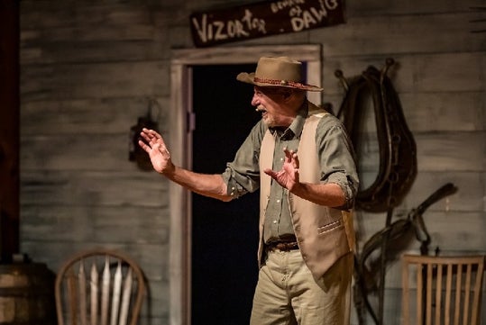 A man in a hat with his hands up and laughing on stage at WhoDunnit Hoedown Murder Mystery Dinner Show in Branson, Missouri.
