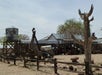 Wide shot of several old buildings, trees, water tower, and other western themed items on display on a sunny day.