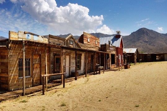 The front of several wooden buildings with small awnings with the sun beating down on the on the Wild West Ghost Tour.