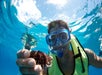 A person wearing a snorkeling mask and life vest holds a sea urchin underwater while looking at the camera.