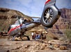 A helicopter is parked on rocky terrain near a group of people sitting at a picnic table in a desert canyon landscape.