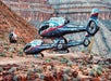 Three helicopters with "Maverick" branding are landed on rocky terrain in a canyon, with cliffs and sparse vegetation in the background.