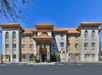 Three-story hotel with a stone entrance, arched windows, and a red-tiled roof, located under a clear blue sky.
