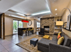 Modern living room with stone fireplace, gray sectional sofa, and large rug. Red pendant light hangs over a high table with chairs. Walls have built-in shelves and clock decor.