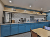 Buffet area with blue cabinets, a countertop, and a tiled backsplash. Includes serving station, trays, and shelves with dishes and fruit. A table and chairs are in the foreground.