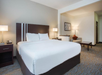 Hotel room with a large bed, two bedside tables with lamps, a sitting area with a sofa and table, and a framed picture on the wall.