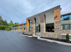 A modern hotel building with stone accents and large windows, featuring orange and brown exterior panels and surrounded by a newly paved parking lot.