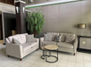A seating area with two beige sofas, patterned pillows, a round nested coffee table, a potted plant, and a floor lamp on a tiled floor.
