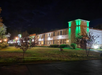 Two-story hotel building with green accent lighting at night, surrounded by trees and grass.