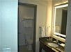 Bathroom with a toilet, towel rack, towels, a sink with a dark countertop, toiletries, and a large illuminated mirror.