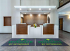 Hotel lobby reception area with two wood-paneled desks and a flower arrangement. Two branded mats on the floor read "Wingate by Wyndham.