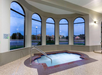 Indoor hot tub with surrounding windows showing an evening outdoor view.