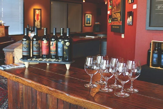 A wooden bar countertop with a display of six bottles of wine and six glasses at Pondera Winery near Seattle, Washington.
