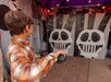 A boy holding a beanbag prepares to play a carnival game, aiming at two panels with large cartoon skull faces.