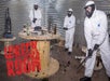 Two men in white suits wearing protective face gear and smashing glass bottle at Wreck Room A Destruction Experience.