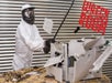 A person in a white protective suit and matching face gear swinging a metal rod destroying things at Wreck Room Las Vegas Printer Smashing Experience.