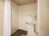 Accessible shower with a wall-mounted bench, grab bar, handheld showerhead, and a white curtain.