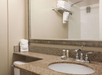 A bathroom with a granite countertop sink, towels hanging above, toiletries next to the faucet, and a view of the shower area with white tiles and a towel rack.