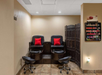 A salon with two black leather pedicure chairs, red pillows, footrests, a carved wooden partition, and a nail polish display on the wall.