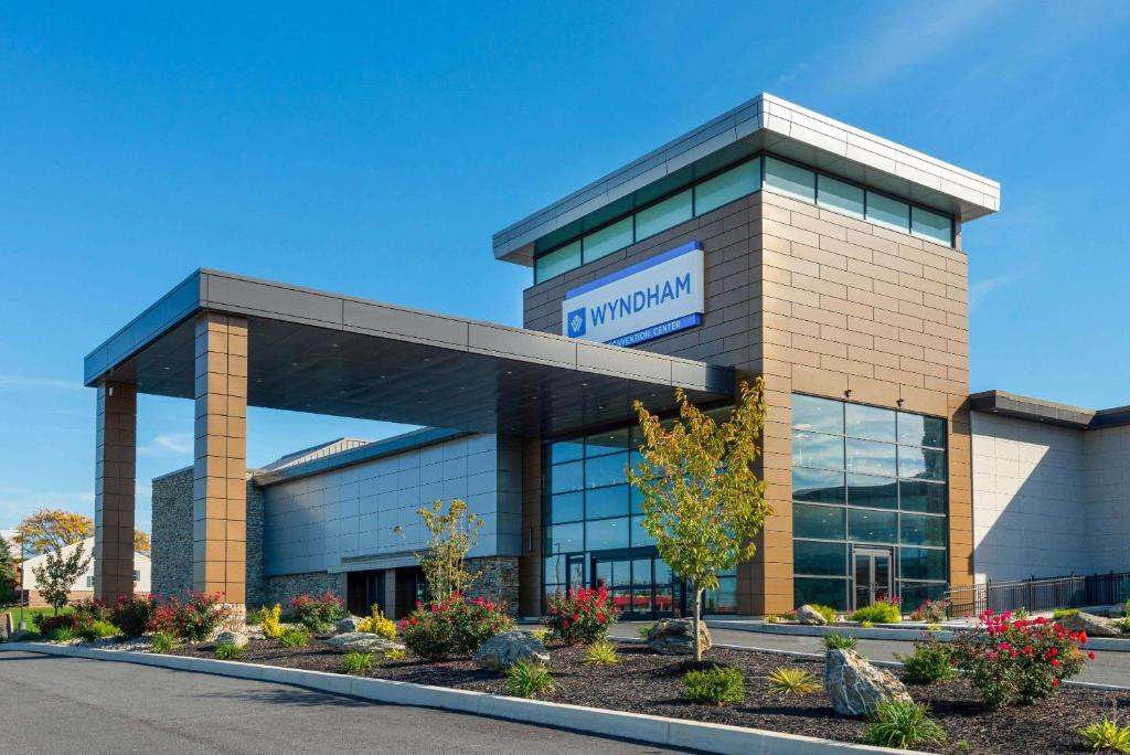 A modern Wyndham hotel entrance with large windows, brick siding, and landscaped surroundings under a clear blue sky.