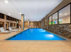 Indoor swimming pool with clear blue water, surrounded by lounge chairs and stone walls, under a white ceiling with ambient lighting.