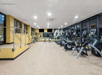 A well-lit gym with cardio machines, weights, and benches. Large windows and mirrors line the walls.