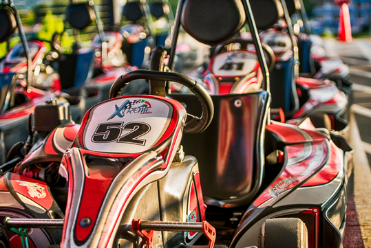 A close-up view of a red and black go-kart with the number 52 on the front, parked among other go-karts in an outdoor track setting.