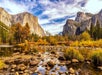Scenic view of a rocky riverbank surrounded by autumn trees and towering granite cliffs under a partly cloudy sky.