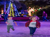 Two young children run on a lit pathway at night, with colorful holiday lights and adults visible in the background.
