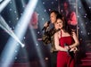 A woman in a red dress and a man in a gold metallic shirt holding microphones and performing on stage at #1 Hits of the 60's.