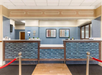 Hotel reception area with a blue and beige color scheme, tiled front desk, red rope barrier, and framed art on the wall.