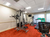 A small gym room with a weight machine, two treadmills, a stationary bike, and a wall-mounted TV on a red carpeted floor.